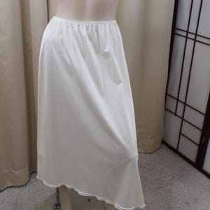 May include: A white slip skirt with a lace trim. The skirt is made of a silky material and has a full, flowing shape.