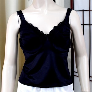 May include: A black camisole with a V-neckline and delicate lace trim. The top has thin straps and a smooth, satin-like texture. The garment is displayed on a mannequin, paired with white bottoms, against a neutral background.