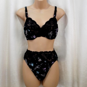 May include: Black lingerie set featuring a bra and high-waisted briefs. The set is adorned with delicate floral embroidery in shades of purple, blue, and white. The bra has scalloped lace trim, and the briefs have a matching lace waistband.