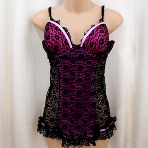May include: Black lace lingerie with a pink bust and trim. The lingerie features a floral lace pattern and thin straps. The bust has a pink lining and a pink ribbon trim. The bottom hem has a ruffled lace edge.