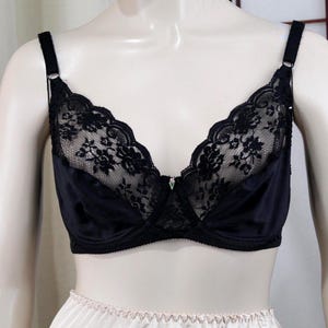 May include: Black bra with lace detailing. The bra features adjustable straps and a classic design. The cups are partially covered with intricate black lace, adding a touch of elegance. The bra is displayed on a mannequin.