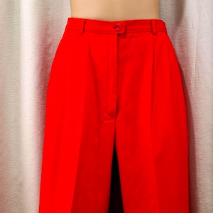 May include: High-waisted trousers in a vibrant solid red color. These pants feature a structured waistband with a single button closure, a central zipper fly, and subtle vertical pleats extending from the waist down the front of each leg.
