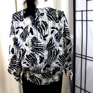 Pu&ograve; includere: Una camicetta a maniche lunghe con un motivo animalier bianco e nero simile a quello di una zebra su uno sfondo testurizzato verde oliva e grigio. Il capo presenta un orlo e polsini elasticizzati arricciati, con scollo rotondo e vestibilit&agrave; ampia.