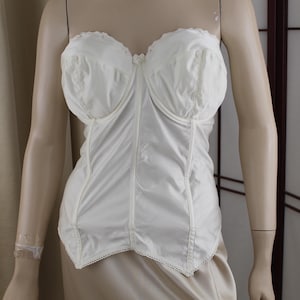 Könnte beinhalten: Elfenbeinfarbenes Bustier mit herzförmigem Ausschnitt und zarter Spitzenborte. Das strukturierte Oberteil hat geformte Cups und eine schmale Taille. Das Kleidungsstück wird auf einer Schaufensterpuppe präsentiert.