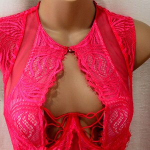 K&ouml;nnte beinhalten: Ein leuchtend pinkfarbenes Dessous-Oberteil mit aufwendigen Spitzendetails. Das &auml;rmellose Oberteil hat ein Schl&uuml;sselloch-Design auf der Vorderseite, mit einem zarten Spitzemuster und einem kleinen Verschluss am Ausschnitt. Das Kleidungsst&uuml;ck wird auf einer Schaufensterpuppe pr&auml;sentiert.