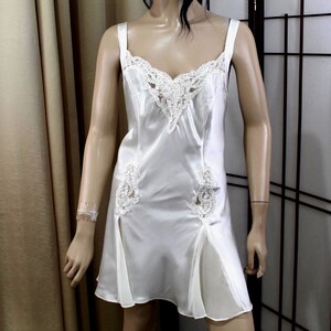 Puede incluir: Un camis&oacute;n de sat&eacute;n blanco con delicados adornos de encaje en el escote y el corpi&ntilde;o. El vestido presenta tirantes finos y detalles de encaje en la falda. El camis&oacute;n es una prenda de lencer&iacute;a cl&aacute;sica.