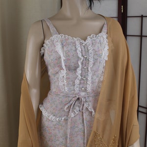 May include: A vintage dress with a floral print and lace trim. The dress has a fitted bodice and a flowing skirt. It is paired with a sheer, gold-coloured shawl.
