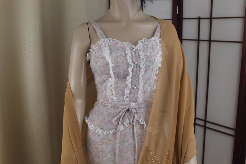 May include: A vintage dress with a floral print and lace trim. The dress has a fitted bodice and a flowing skirt. It is paired with a sheer, gold-coloured shawl.