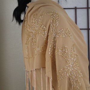 May include: A beige chiffon shawl with gold beaded floral embroidery and fringe trim.
