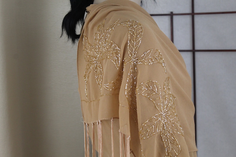 May include: A beige chiffon shawl with gold beaded floral embroidery and fringe trim.