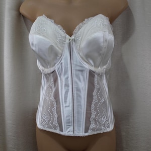 Op de afbeelding: Witte satijnen corset met kanten details. De bustier heeft een sweetheart halslijn en delicate kanten afwerking langs de bovenrand. Het heeft een verticale ritssluiting en doorschijnende kanten panelen. Klassiek lingerie-item.