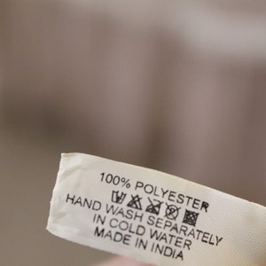 May include: A white fabric care label with black text that reads "100% Polyester, Hand Wash Separately in Cold Water, Made in India". The label also includes a set of universal care symbols.