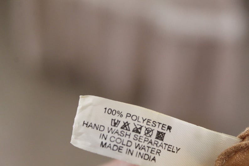 May include: A white fabric care label with black text that reads "100% Polyester, Hand Wash Separately in Cold Water, Made in India". The label also includes a set of universal care symbols.