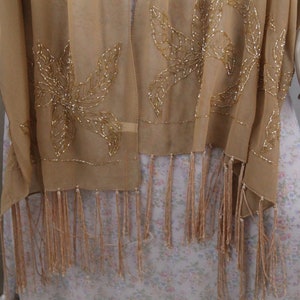 May include: A beige sheer shawl with gold beaded floral embroidery and fringe trim.