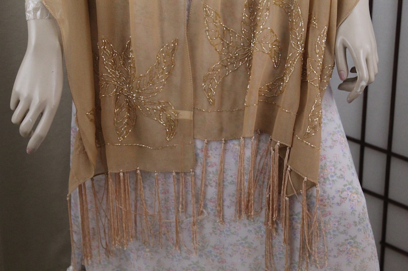 May include: A beige sheer shawl with gold beaded floral embroidery and fringe trim.
