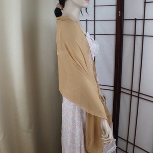 May include: A light brown sheer scarf draped over a person's shoulders. The scarf is made of a soft, flowing fabric and has a simple, elegant design.