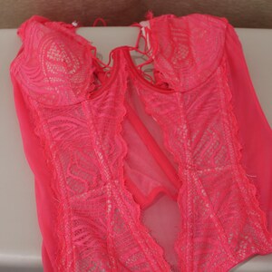 K&ouml;nnte beinhalten: Ein leuchtend pinkfarbenes Dessous-Set mit einem Spitzenmieder und transparenten Eins&auml;tzen. Das Kleidungsst&uuml;ck hat ein zartes Spitzendesign und eine schmeichelhafte Silhouette. Die Dessous sind mit verstellbaren Tr&auml;gern und einer bequemen Passform ausgestattet.