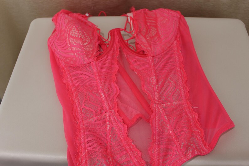 K&ouml;nnte beinhalten: Ein leuchtend pinkfarbenes Dessous-Set mit einem Spitzenmieder und transparenten Eins&auml;tzen. Das Kleidungsst&uuml;ck hat ein zartes Spitzendesign und eine schmeichelhafte Silhouette. Die Dessous sind mit verstellbaren Tr&auml;gern und einer bequemen Passform ausgestattet.