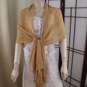 May include: A gold sheer shawl with a beaded fringe. The shawl is draped over a mannequin and tied at the neck.