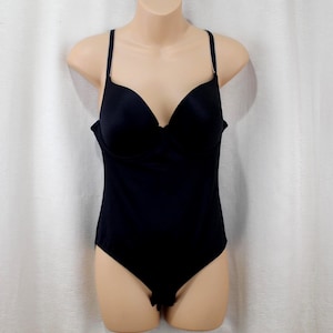 May include: A black bodysuit with a built-in bra and adjustable spaghetti straps. The one-piece garment has a deep V-neckline and a smooth, seamless design. The bodysuit is displayed on a mannequin.