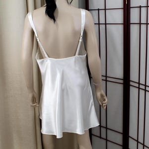 Puede incluir: Vestido lencero de sat&eacute;n color marfil con tirantes finos ajustables. El vestido tiene una silueta fluida en forma de A y una espalda baja. La tela tiene un brillo sutil. El vestido se exhibe en un maniqu&iacute;.