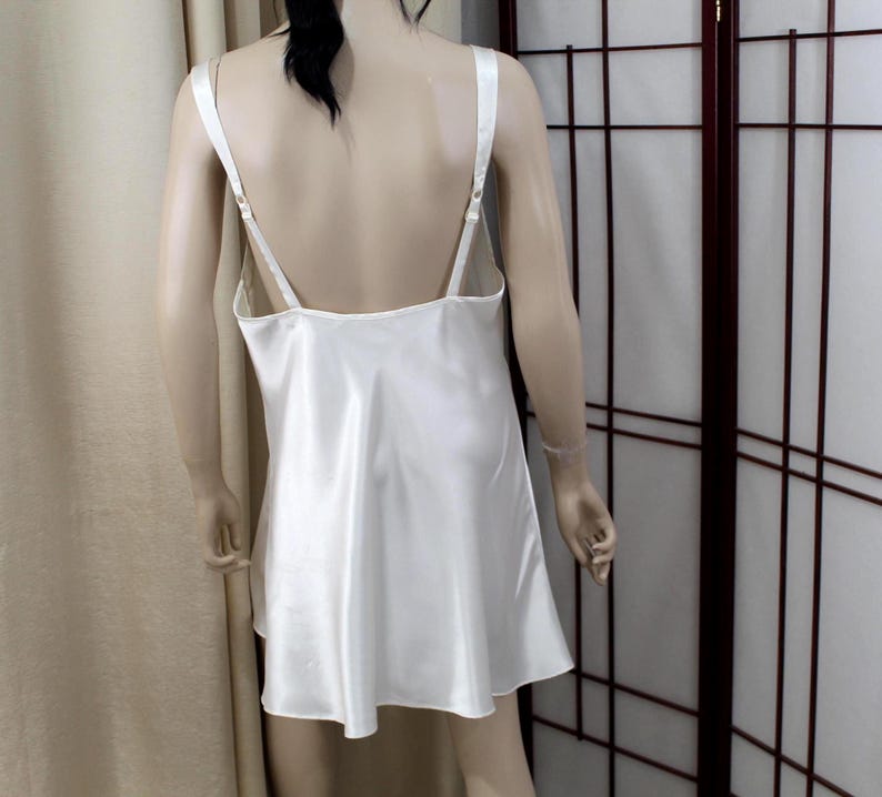 Puede incluir: Vestido lencero de sat&eacute;n color marfil con tirantes finos ajustables. El vestido tiene una silueta fluida en forma de A y una espalda baja. La tela tiene un brillo sutil. El vestido se exhibe en un maniqu&iacute;.
