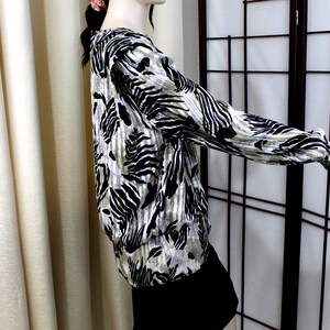 Pu&ograve; includere: Una camicetta a maniche lunghe caratterizzata da un audace motivo animalier ispirato alla zebra, nei toni del nero e del beige. Il capo presenta uno scollo rotondo, maniche lunghe con polsini aderenti e un orlo leggermente arricciato in vita.