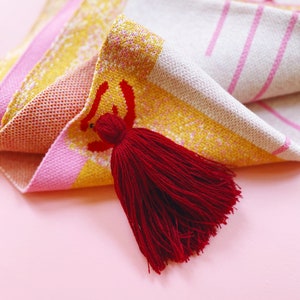 May include: A pink, yellow, and white woven blanket with a red tassel. The blanket has a geometric pattern.