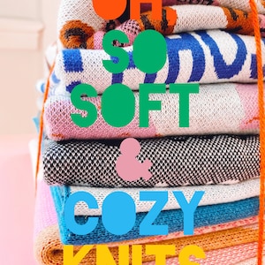 May include: A stack of colorful knit blankets with the text "OH SO SOFT & COZY KNITS" in large, colorful letters.