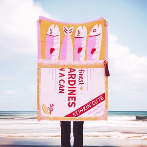 May include: Pink and yellow beach towel with a graphic of a can of sardines. The can says "finest sardines in a can" and "stinkin' cute".
