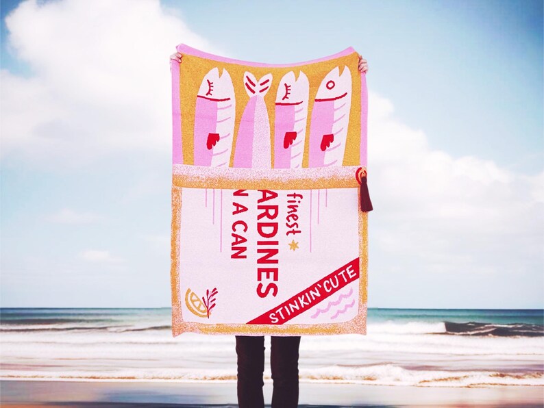 May include: Pink and yellow beach towel with a graphic of a can of sardines. The can says "finest sardines in a can" and "stinkin' cute".