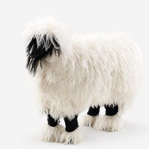 May include: A decorative sheep-shaped stool covered in long, shaggy white faux fur. The animal figure features a solid black face with a pointed snout and black lower legs that contrast with the white fur on the hooves and the main body.