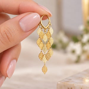 May include: A gold-toned dangle earring featuring a small hoop closure attached to a cascading arrangement of multiple textured leaf-shaped charms. The charms are arranged in a tiered, overlapping pattern, creating a layered effect.