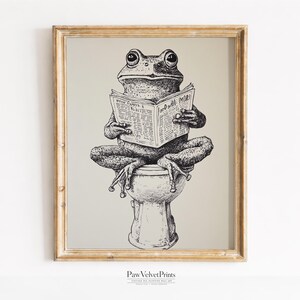 May include: A framed black and white ink illustration of a frog sitting on a toilet while reading a newspaper. The frog is depicted in a seated position with its legs crossed, holding an open newspaper with text visible on the pages.