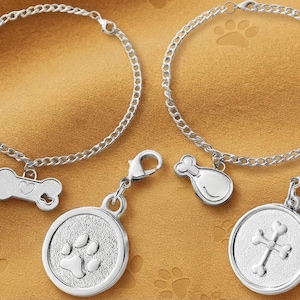 May include: Two silver-toned metal chain bracelets with lobster clasps. One bracelet features a bone-shaped charm with a heart cutout, and the other has a drumstick charm. Two additional round charms feature a paw print and a cross-bone design.