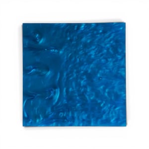 Puede incluir: Un posavasos cuadrado de resina azul con un patrón arremolinado y veteado. El color es un azul profundo y vibrante con reflejos azules más claros, creando un efecto visual dinámico y fluido. El posavasos es una superficie sólida y lisa.