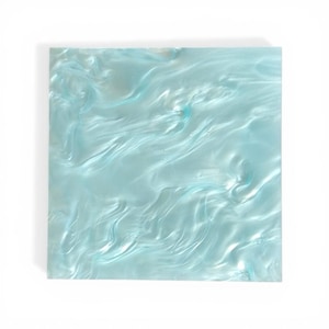 Peut inclure: Plaque carrée en acrylique bleu clair avec un motif nacré et tourbillonnant. La surface a une finition brillante, avec des tons bleu clair et foncé créant un effet fluide semblable à l'eau. Les bords sont nets.