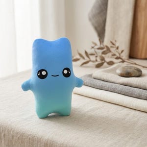 May include: A soft plush toy shaped like a stylized figure with a smooth blue gradient finish. The figure features a simple, rounded body with two small arms and two legs, and a face with two large black eyes with white highlights and a small smile.