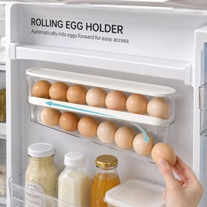 May include: A white and clear plastic rolling egg holder mounted inside a refrigerator. The unit features two tiers for storing brown eggs, with text reading ROLLING EGG HOLDER and Automatically rolls eggs forward for easy access.