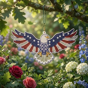 Può includere: Un ornamento decorativo a forma di aquila con le ali spiegate, con un design patriottico con colori rosso, bianco e blu. L'ornamento è appeso a un filo verde su uno sfondo di fiori e fogliame.