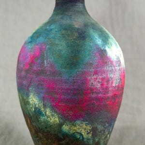 May include: A ceramic vase with a rounded body and a narrow neck. The vase is decorated with a colorful abstract design in shades of blue, green, pink, and purple.