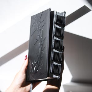 May include: A black Bible with embossed botanical design and labeled tabs. The book is held open, revealing the pages and chapter markers. The word "Joseph" is embossed on the cover.