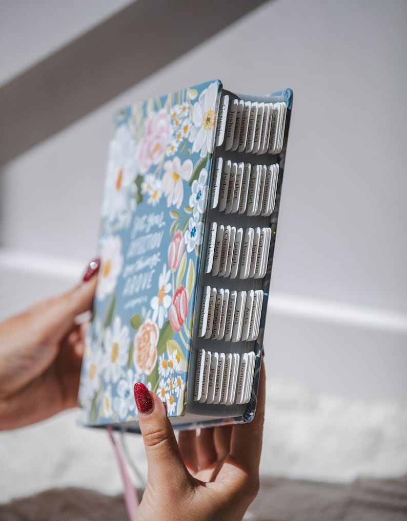 K&ouml;nnte beinhalten: Ein Buch mit hellblauem Einband, verziert mit wei&szlig;en, rosa und orangefarbenen Blumenmustern. Das Buch hat beschriftete Registerkarten und den Text "Do you fix your affection on things above". Das Buch wird offen gehalten.