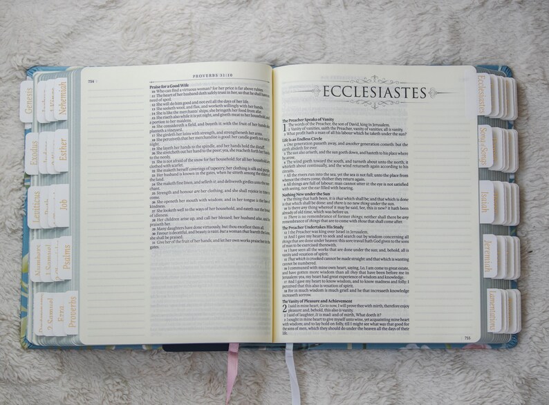 K&ouml;nnte beinhalten: Ge&ouml;ffnete Bibel mit beschrifteten Registerkarten. Das Buch ist zum Buch Kohelet aufgeschlagen. Die Seiten sind cremefarben mit schwarzem Text. Der Einband ist blau mit floralem Muster. Registerkarten sind mit Buchnamen beschriftet.