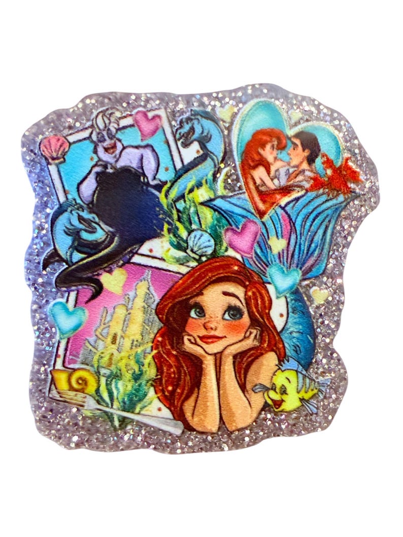 May include: A glittery, multi-colored resin charm featuring scenes from The Little Mermaid. The charm includes images of Ariel, Ursula, and other characters, with heart and seashell accents. The border is silver glitter.