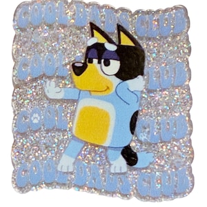 May include: A glittery, square-shaped pin featuring a cartoon dog in a blue and yellow outfit. The pin has the words "COOL DADS CLUB" in light blue around the edges. The dog is striking a pose with one arm up.