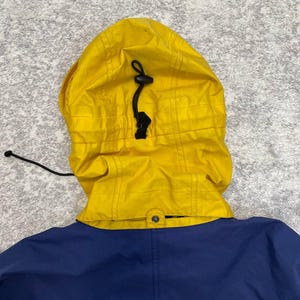 May include: A bright yellow hood with a black drawstring and toggle adjustment attached to a solid navy blue jacket. The hood features a grid-like ripstop texture and is connected to the collar with a single visible snap button at the center.