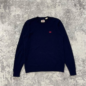 May include: A navy blue long-sleeve sweater with a crew neckline and ribbed cuffs and hem. The garment features a small red Levi's brand logo patch on the left chest and a white interior neck label with the Levi's brand name printed in red.
