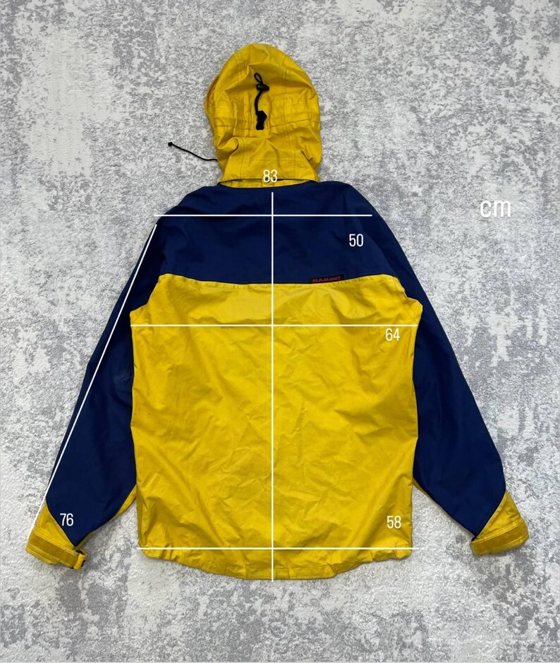 May include: A yellow and navy blue hooded jacket with long sleeves and a drawstring hood. White measurement lines and numbers indicate a length of 83 cm, a shoulder width of 50 cm, a chest width of 64 cm, and sleeve lengths of 76 cm and 58 cm.