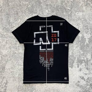 K&ouml;nnte beinhalten: Ein schwarzes Kurzarm-T-Shirt mit einer wei&szlig;en und roten Grafik auf der R&uuml;ckseite. Das Design zeigt ein stilisiertes Kreuz-Logo, den Text 2017 und eine Liste von Tourdaten. Wei&szlig;e Messlinien und Zahlen in cm sind &uuml;ber das Kleidungsst&uuml;ck gelegt.